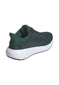 Zapatilla deportiva de malla verde con un cuello acolchado, cierre de cordones y una suela blanca acolchada. Presenta tres franjas horizontales oscuras en el lateral.