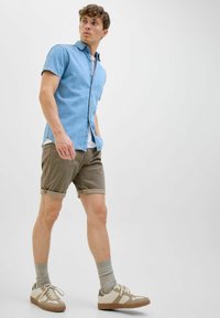 Lyseblå denim skjorte med korte ærmer, khaki shorts med opsmøg, grå sokker og beige sneakers med hvide detaljer. Enkel og moderne design.