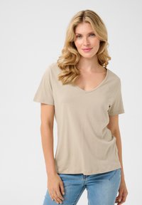 Beige v-hals t-shirt lavet af blødt stof, med korte ærmer og en afslappet pasform, parret med lyseblå denimjeans.