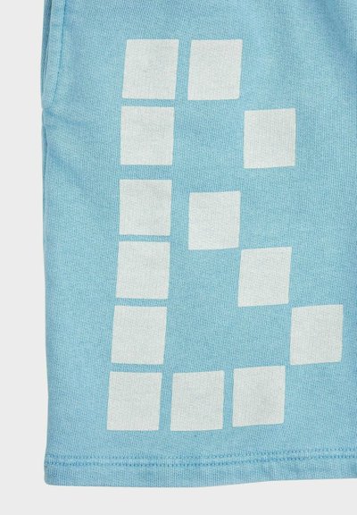 Tissu bleu clair avec un motif de carrés blancs disposés en grille décalée dans le coin inférieur.