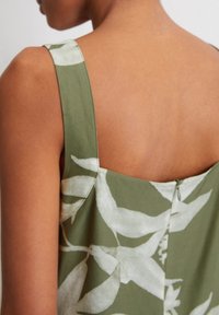Grünes Kleid mit Blumenmuster; hat breite Träger, einen quadratischen Rücken und ein dezentes Knopfdetail am Halsausschnitt. Glatte Stofftextur.