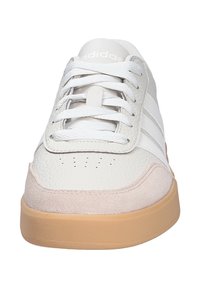 White athletic shoe with textured leather upper, soft pink suede accents, white laces, and a gum rubber outsole. Features perforated toe.