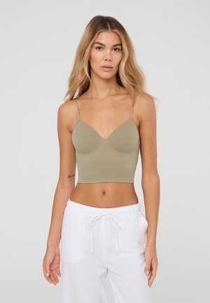 Top corto a righe, verde oliva, con spalline sottili regolabili e scollatura profonda, abbinato a pantaloni bianchi con coulisse.