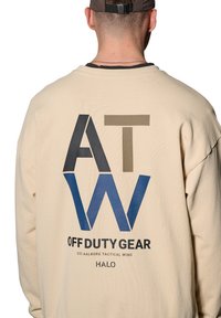 Beżowa bluza z dużymi nadrukowanymi literami "ATW" w ciemnoniebieskim, czarnym i oliwkowym kolorze, tekstem "OFF DUTY GEAR" i logo poniżej. Miękka tekstura materiału.