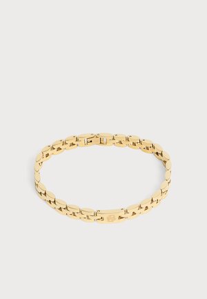 Guld kæde armbånd med ovale led og en rektangulær lås med et lille graveret design, vist på en lys baggrund.