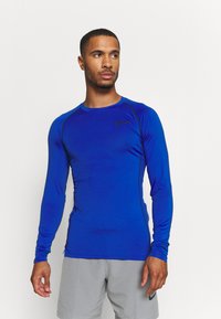 Langärmliges Sportshirt in leuchtendem Blau mit schwarzen Akzenten. Verfügt über ein tailliertes Design und einen glatten, dehnbaren Stoff. Logo auf der Brust.
