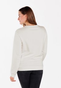 Felpa grigia chiara con scollatura a girocollo, maniche lunghe e polsini a costine. Texture morbida e design semplice, abbinata a jeans scuri.