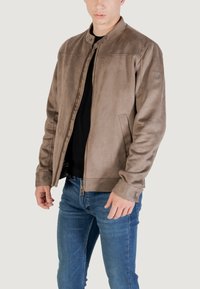 Giacca in ecopelle marrone con colletto rialzato, zip frontale e tasche laterali. Presenta una texture liscia e dettagli di cucitura sottili.