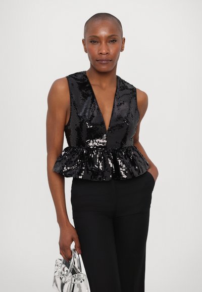 Must have kahehõlmadega must särk sügava V-kaelusega, sädelev tekstuur ja peplum vöökoht. Seljas mustad püksid, hoides läbipaistvat kotti.