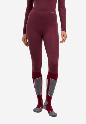 Close-up af en person iført tætsiddende vinrøde leggings og vinrøde og grå knæstrømper med et tekstureret design.