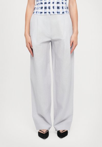Lichtgrijze wijde broek van stof met een zachte textuur. Voorzien van voorkreukels en een relaxte pasvorm, gecombineerd met zwarte puntige schoenen.