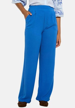 Person wearing bright blue high-waist wide-leg pants with side pockets, a white shirt with blue embroidery, and brown moccasin shoes.