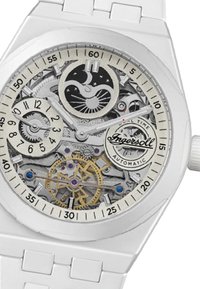 Weiße automatische Uhr mit einem transparenten Ziffernblatt, das mechanische Zahnräder zeigt, goldene Akzente und blaue Schmuckdetails aufweist. Numerische und Stundenmarkierungen sind vorhanden.