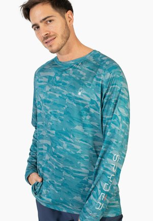 Langärmliges türkisfarbenes Shirt mit geometrischem Muster, aus leichtem Material gefertigt. Verfügt über ein Logo auf der oberen Brust und vertikalem Text auf dem Ärmel.