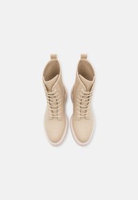 Bottes montantes en toile beige avec lacets, bout arrondi et languettes à l'arrière, vues de dessus sur fond blanc.
