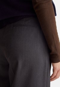 Szare spodnie o dopasowanym kroju z gładkim wykończeniem, z płaską kieszenią, zestawione z brązowym swetrem z dzianiny. Widoczna fakturowana tkanina.