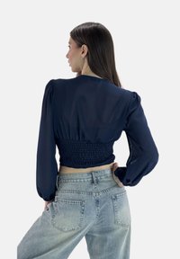 Marineblaues, kurz geschnittenes Oberteil mit langen Ärmeln, gerafftem Rücken und glattem Stoff, kombiniert mit hochtaillierten hellblauen Jeans.