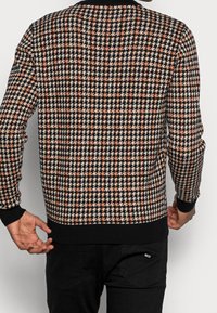 Maglione lavorato a maglia con un motivo a pied de poule in nero, beige e arancione, con polsini e orlo a costine neri. Vista posteriore mostrata.