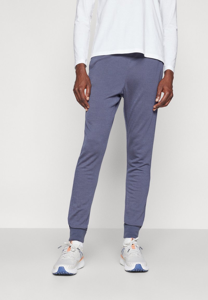 Dark blue joggers made of soft fabric, featuring a slim fit and ribbed cuffs. Paired with grey athletic shoes with orange accents.