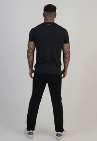 Tricou negru cu dungi, cu mâneci scurte și guler rotund; asortat cu pantaloni negri și adidași gri; tatuaje vizibile pe brațe.