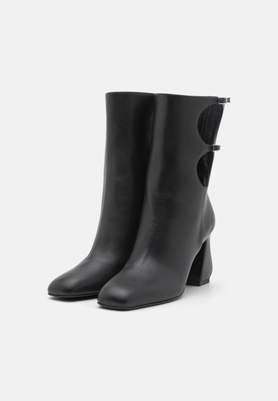 Black leather ankle boots with a block heel, featuring a smooth texture and cut-out side details secured by small metallic clips.