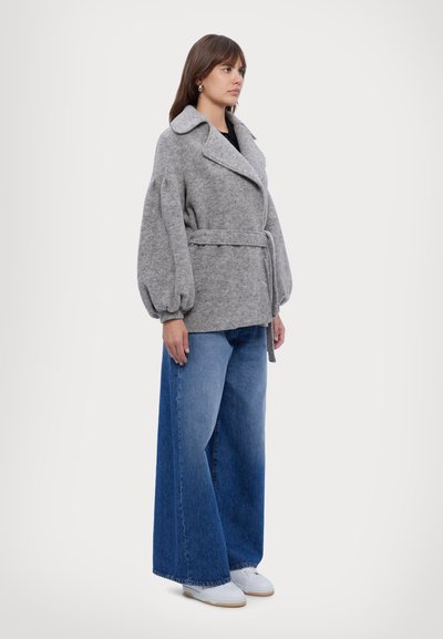Manteau en laine gris avec un large col, design enveloppant et taille ceinturée ; associé à un jean en denim bleu ample et des baskets blanches.