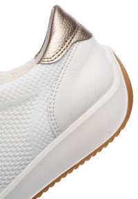 Nahaufnahme der Ferse eines weißen Sneakers mit strukturiertem Strickstoff, metallischem bronzenem Lederdetail, weißer Sohle und Gummiaußensohle.