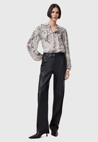 Lys grå mønstret bluse med sort blomsterdesign, parret med højtragtede sorte læderbukser og spidse sorte hæle.