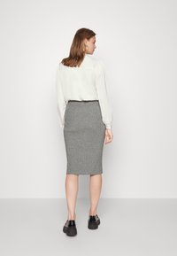 Grijze geribbelde kokerrok gecombineerd met een witte blouse. De rok heeft een getailleerde pasvorm en een elastische tailleband. Zwarte schoenen maken de look af.