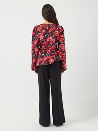 Blumiges Peplum-Top mit lebhaften roten und rosa Blumenmustern auf schwarzem Hintergrund, kombiniert mit schwarzen weiten Hosen. Detail mit Schlüssellochausschnitt im Rücken.