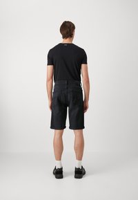 Camisa negra de manga corta combinada con pantalones cortos de mezclilla oscuros. Los pantalones cortos presentan dobladillos enrollados, bolsillos traseros y un acabado liso y texturizado.