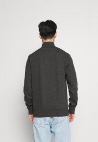 Tmavě šedý svetr s vysokým límcem a žebrovanými manžetami. Vyroben z měkké tkaniny, má jednoduchý design bez viditelných vzorů.