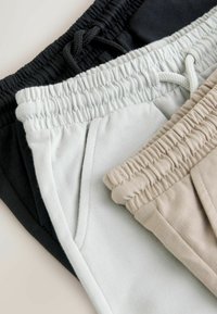 Drei Jogginghosenpaare: schwarz, hellgrau und beige. Jede hat einen elastischen Bund und Seitentaschen, mit einer weichen, glatten Textur.