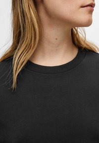 T-shirt en coton noir avec un col rond, doté d'une texture lisse et d'un design simple, montrant une partie du cou et de l'épaule.