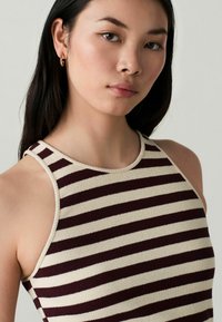 Top senza maniche a righe bordeaux e crema, con scollo rotondo e texture a costine. Design semplice senza accenti o componenti prominenti.