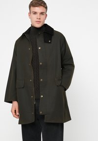 Donkergroene waterdichte jas met een zwarte corduroy kraag, drukknoopsluiting, twee voorzakken en een relaxte pasvorm.