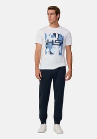 Camiseta blanca de manga corta con un gráfico geométrico azul y el texto "Hackett Sport", combinada con pantalones joggers navy y zapatillas blancas.