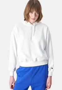 Felpa bianca con una vestibilità comoda, polsini a coste e cappuccio con cordino. Caratterizzata da un piccolo logo sul petto e sul polsino. Abbinata a pantaloni jogger blu.