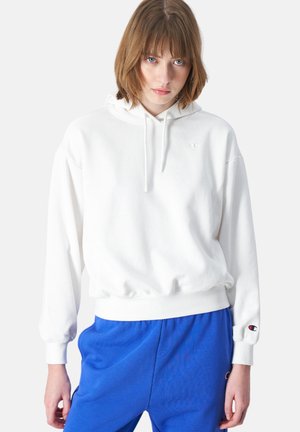 Felpa bianca con una vestibilità comoda, polsini a coste e cappuccio con cordino. Caratterizzata da un piccolo logo sul petto e sul polsino. Abbinata a pantaloni jogger blu.