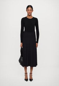 Top negro de mangas largas combinado con una falda midi oscura y fluida, acentuado por unos tacones de aguja negros y un bolso negro texturizado.