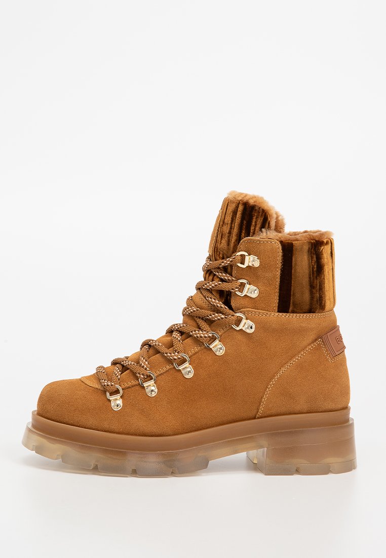 Braune Wildleder-Ankle-Boots mit dicker durchsichtiger Sohle, gepolstertem Kragen, Metall-Ösen und hellbraunen Schnürsenkeln vor weißem Hintergrund.