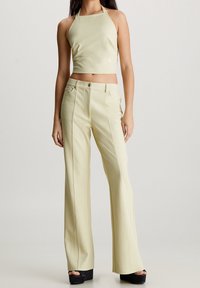 Top corto de tirantes color verde claro combinado con pantalones de talle alto y acampanados en un tono a juego, que presentan líneas limpias y una textura suave.