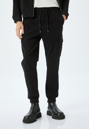 Zwarte cargobroek met een elastische tailleband, zijzakken en elastische boorden, gemaakt van een duurzame stof. gedragen met zwarte enkelboots.