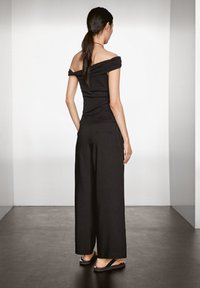 Zwarte off-shoulder top gecombineerd met zwarte wijde broek. De stof lijkt glad, met een eenvoudig, minimalistisch ontwerp en zonder zichtbare patronen.