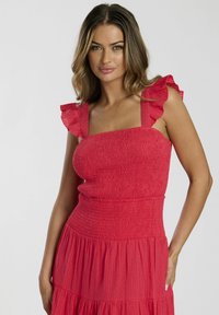 Röd, smockad klänning med volangärmar och en lager-p�å-lager kjol. Tillverkad av lättviktig tyg, med subtil textur och en figurnära bodice.