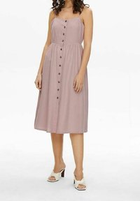 Rosa midiklänning med tunna remmar, har en knappfront, samlad midja och en flödande kjol. Matchas med vita klackskor.