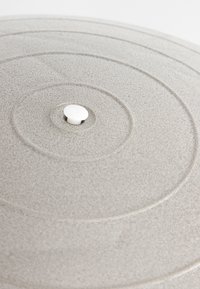 Pyöreä beige tekstuurinen kansi, jossa on keskeiset pyörimisviivat ja pieni valkoinen nuppikahva keskellä.