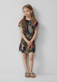 Blumenmuster-Kleid mit Rüschensäumen, dunkelblauem Hintergrund und leuchtenden orange und grünen Akzenten. Kombiniert mit hellbeigen Sandalen.