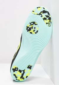 Podeszwa czarno-miętowego buta sportowego z okrągłym wzorem chwytu, falistą fakturą i jaskrawymi żółtymi akcentami, z detalicznym wzorem bieżnika.