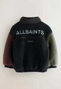 Juodas, žalias ir bordo polarinis džemperis su aukštu apykakle ir elastingomis rankovėmis. Papuoštas balta siuvinėta prekinio ženklo logo nugaroje.